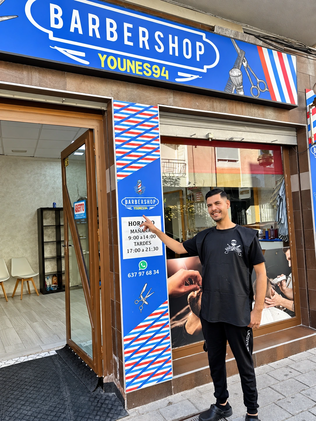 Younes frente a la fachada azul, roja y blanca de Younes 94 Barbershop